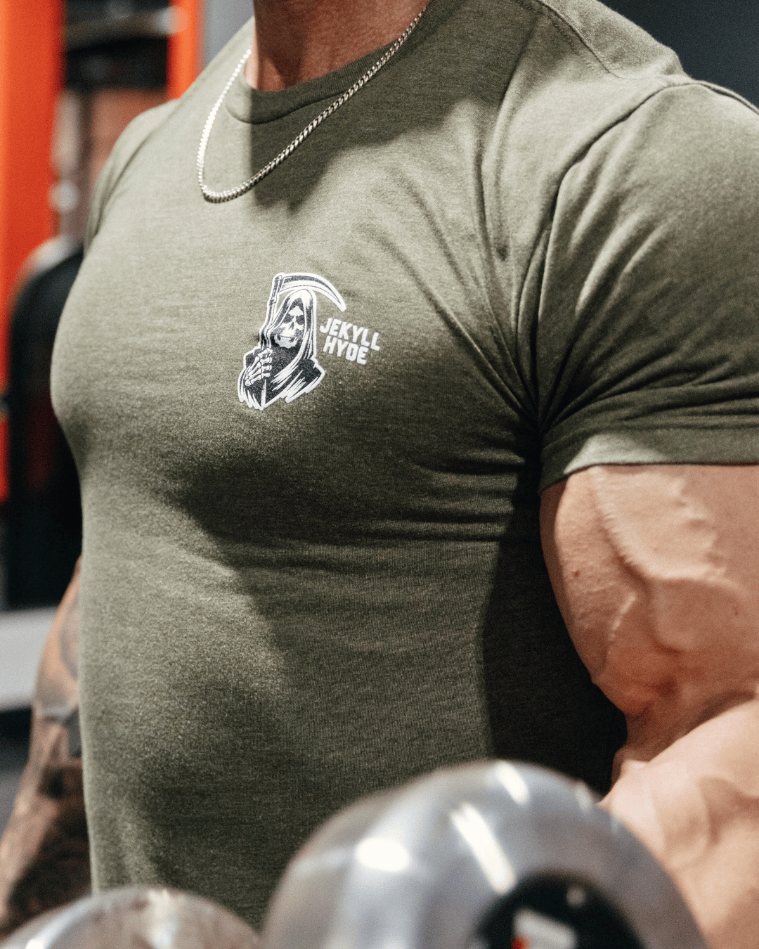 Person wearing a green t-shirt with a logo, lifting weights in a gym setting.