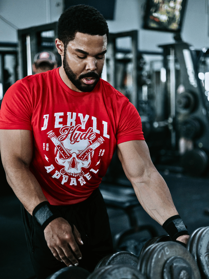 Man grabbing a dumbbell wearing a red shirt with a skull on the front. 