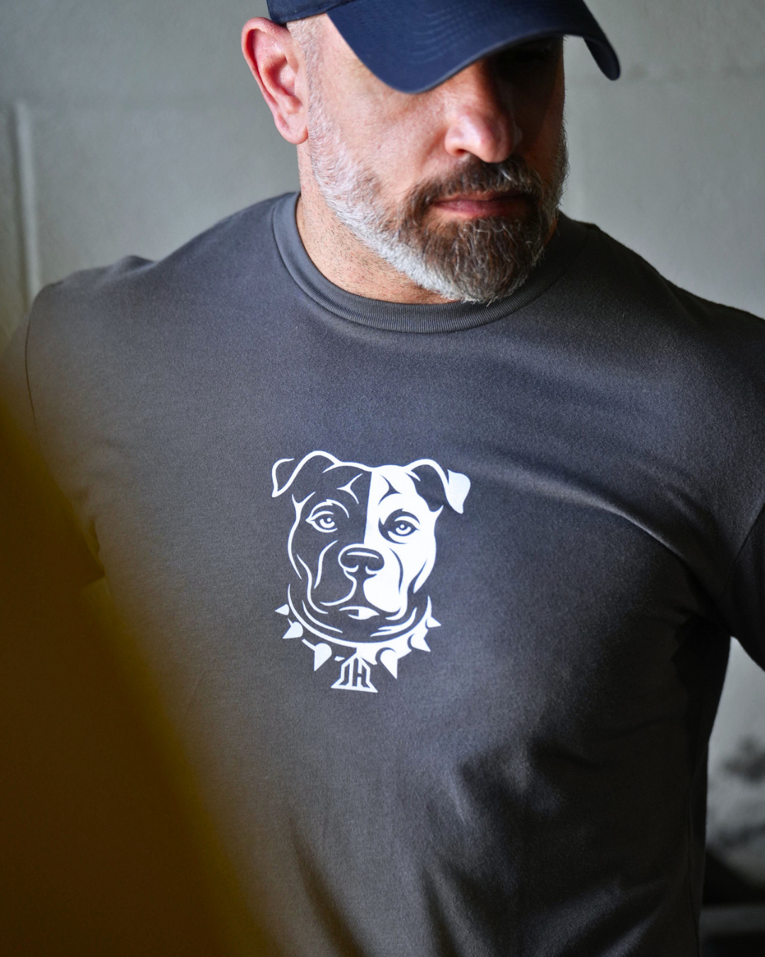 A man wearing a dark gray crewneck t-shirt with a white graphic of a pitbull dog's face, paired with a navy blue baseball cap.