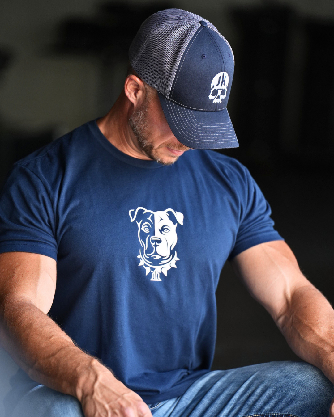 A man sitting looking down wearing a Navy shirt with a Pitbull on it. 