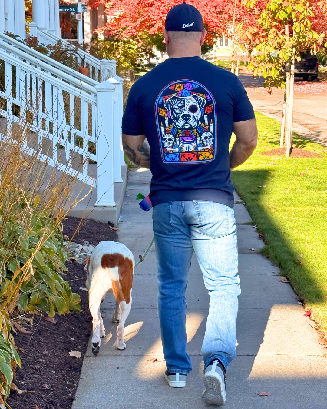 Muscular man walking a dog with a navy shirt with a pitbull ofrenda on the back. 