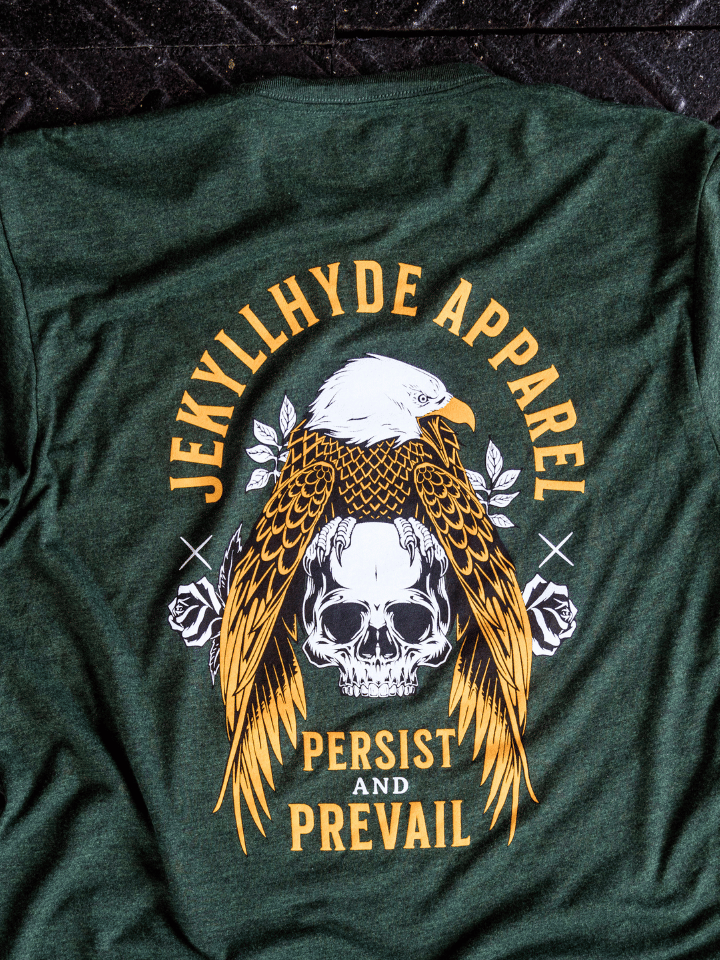 Green tshirt with an eagle and skull on it laying on the ground. 
