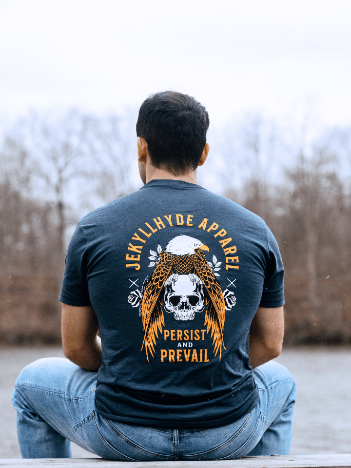 Man sitting outside on a picnic table wearing a tshirt with an eagle and skull on it. 