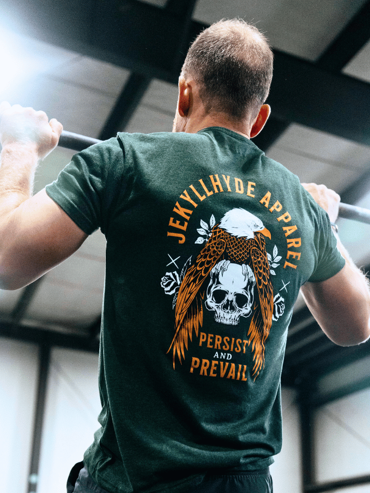 Man doing pullups wearing a green shirt with an eagle and skull on it. 
