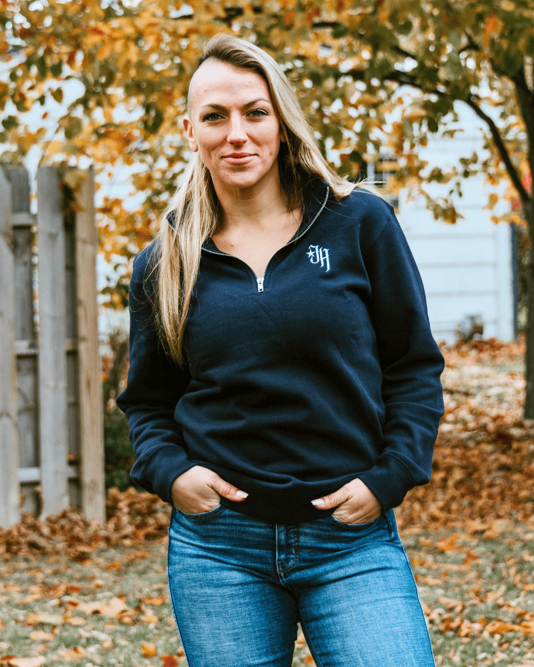 Woman looking into the camera wearing a navy quarter zip sweatshirt. 