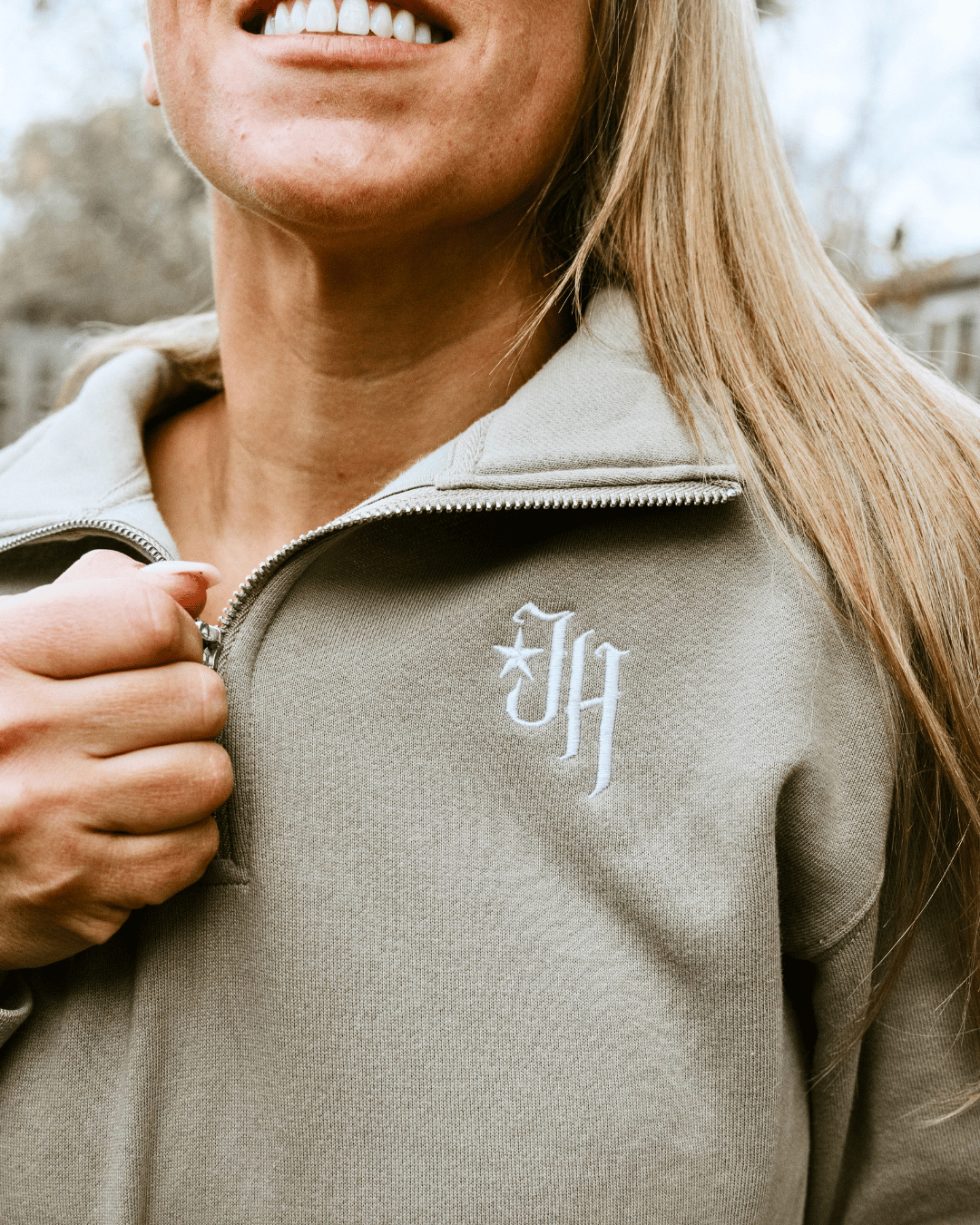 Woman zipping up a zipper on a tan quarter zip sweater. 