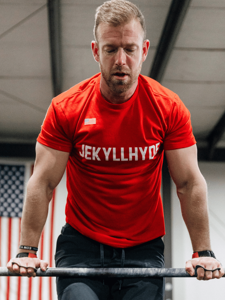 Man on top of a pullup bar in a red Jekyllhyde tshirt. 
