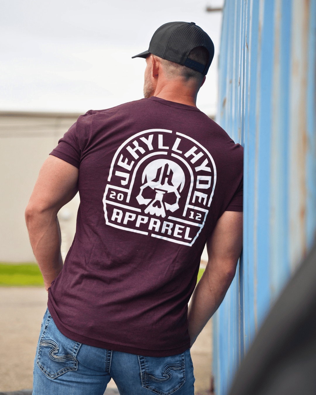 man leaning on a wall wearing a tshirt with a skull on the back. 