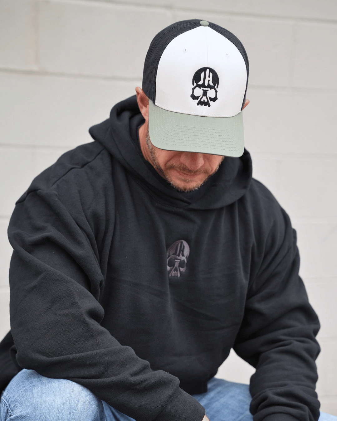 Man looking down wearing a black/cream/ODgreen hat with skull on it. 