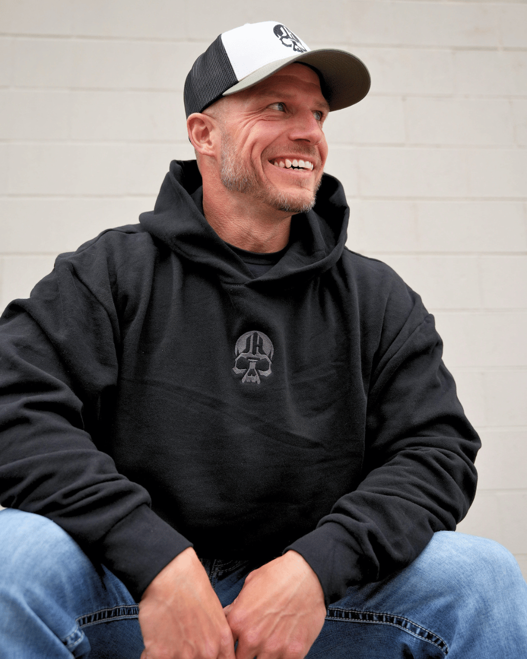 Man smiling in a black hoodie with a skull embroidered on it. 