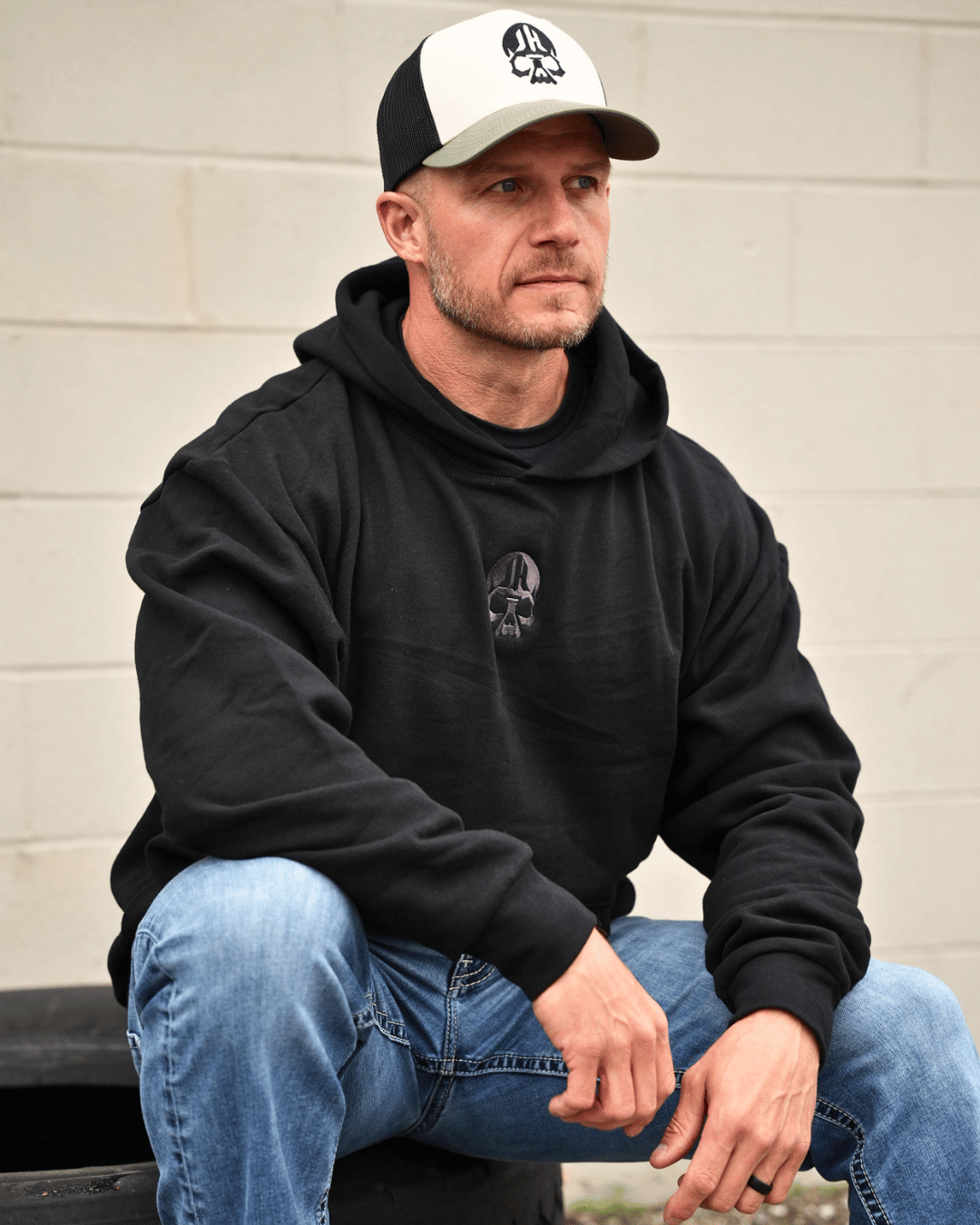 Man sitting on a tire wearing a black hoodie. 