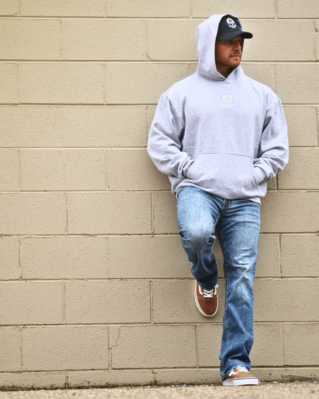 Man standing against a wall wearing a grey hoodie. 