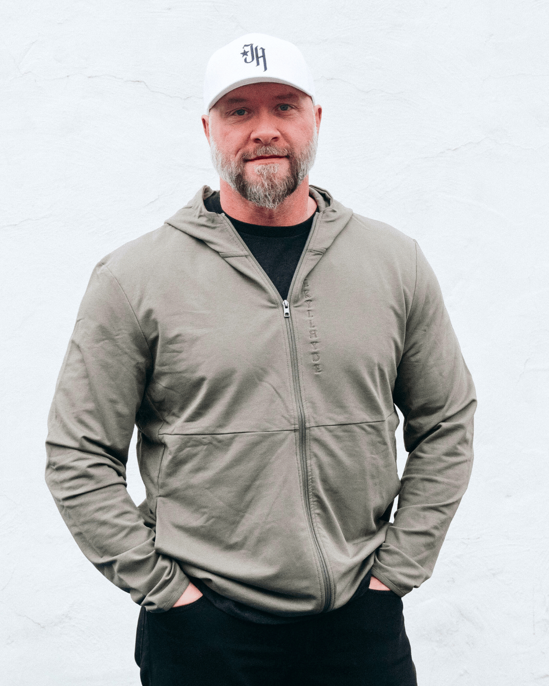 Muscular man standing in tan jacket with a white background. 
