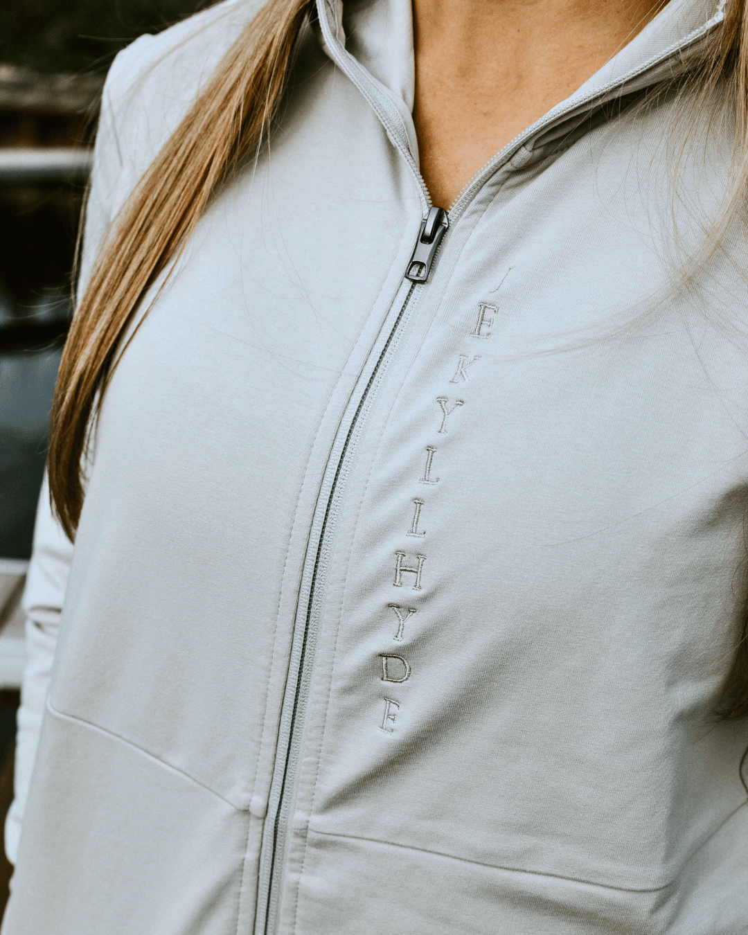 Close up of a tan jacket zipper with vertical Jekyllhyde logo embroidery. 