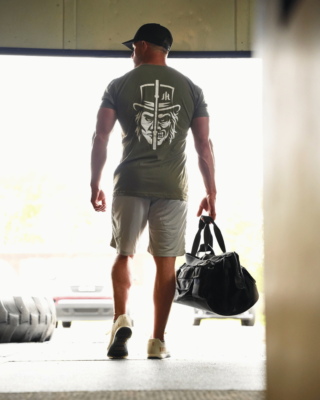 Muscular man walking out of a gym wearing a OD green shirt with a two faced design. 