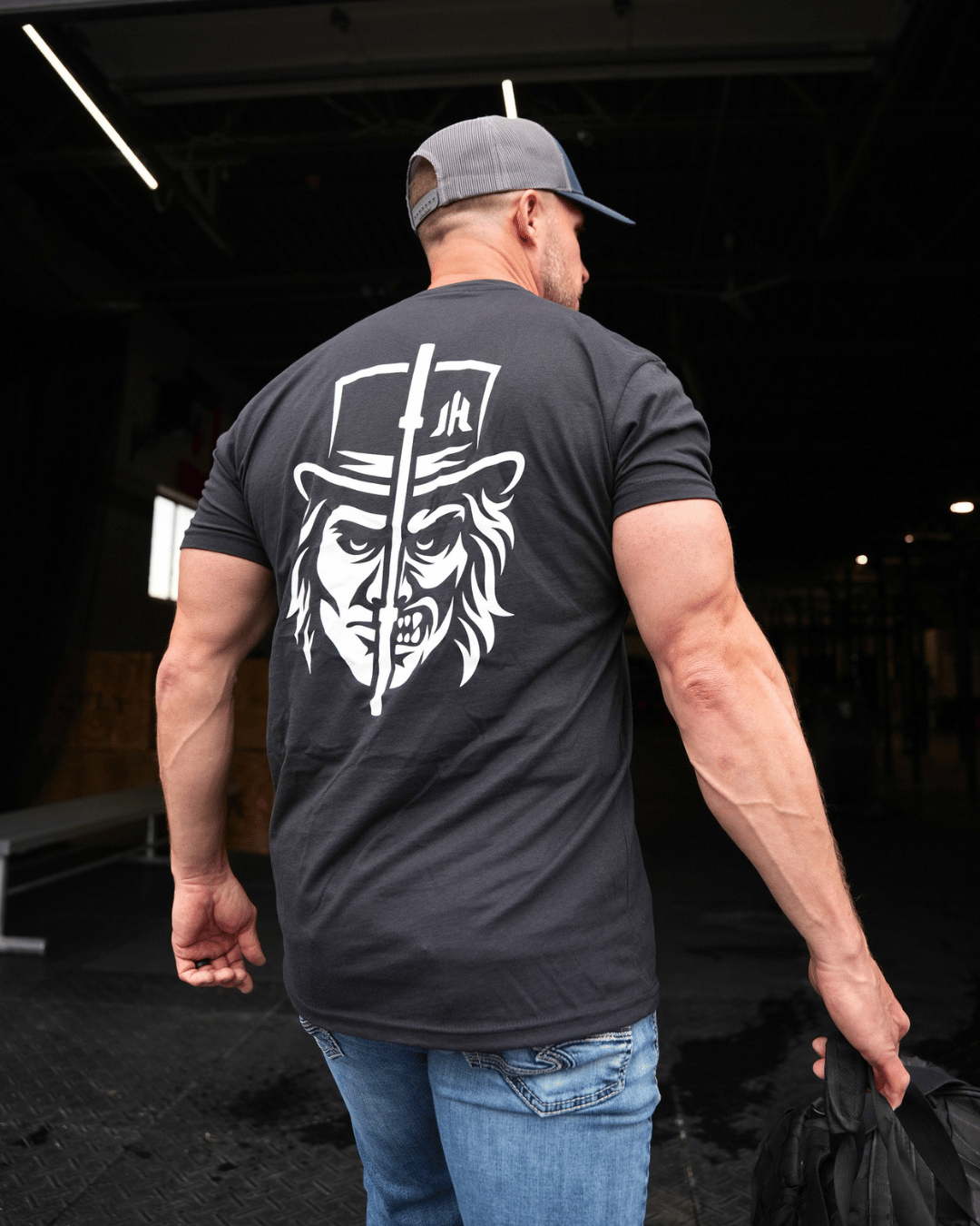 Muscular man walking into a gym wearing a black shirt with a two faced design. 