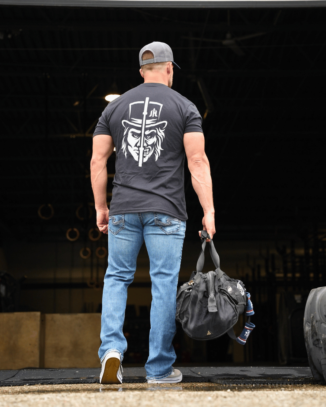 Muscular man walking into a gym wearing a black shirt with a two faced design. 