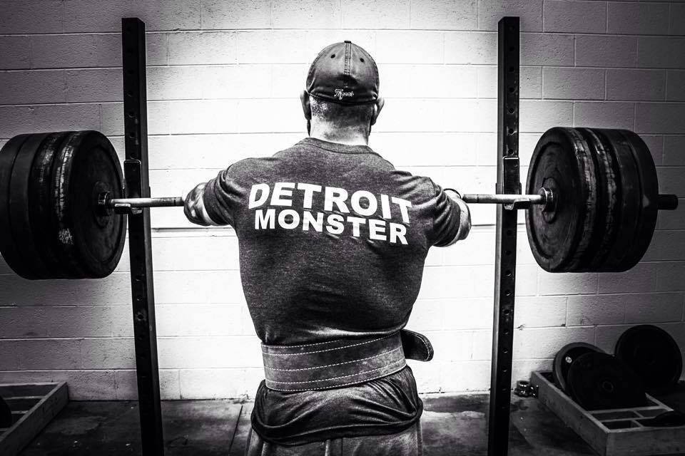 Man standing at a loaded squat rack with a Detroit Monster t-shirt on. 