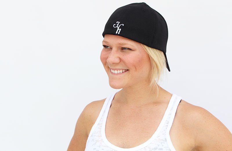Woman smiling off into the distance wearing a backwards black baseball hat. 