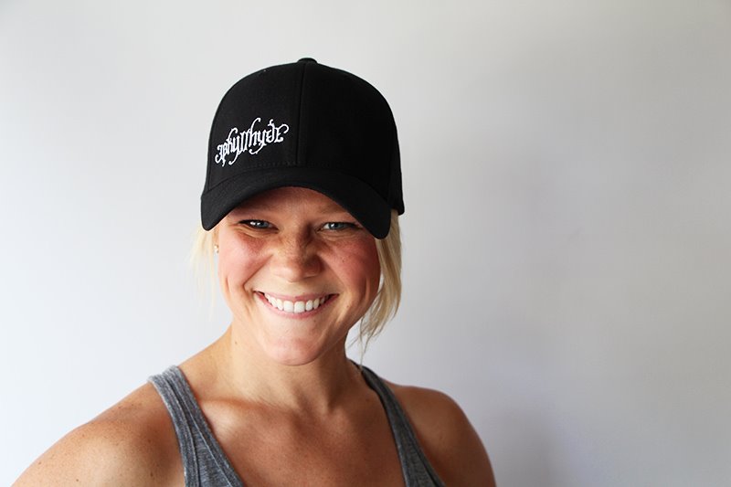Woman smiling into the camera wearing a black baseball cap with a white Jekyllhyde logo. 