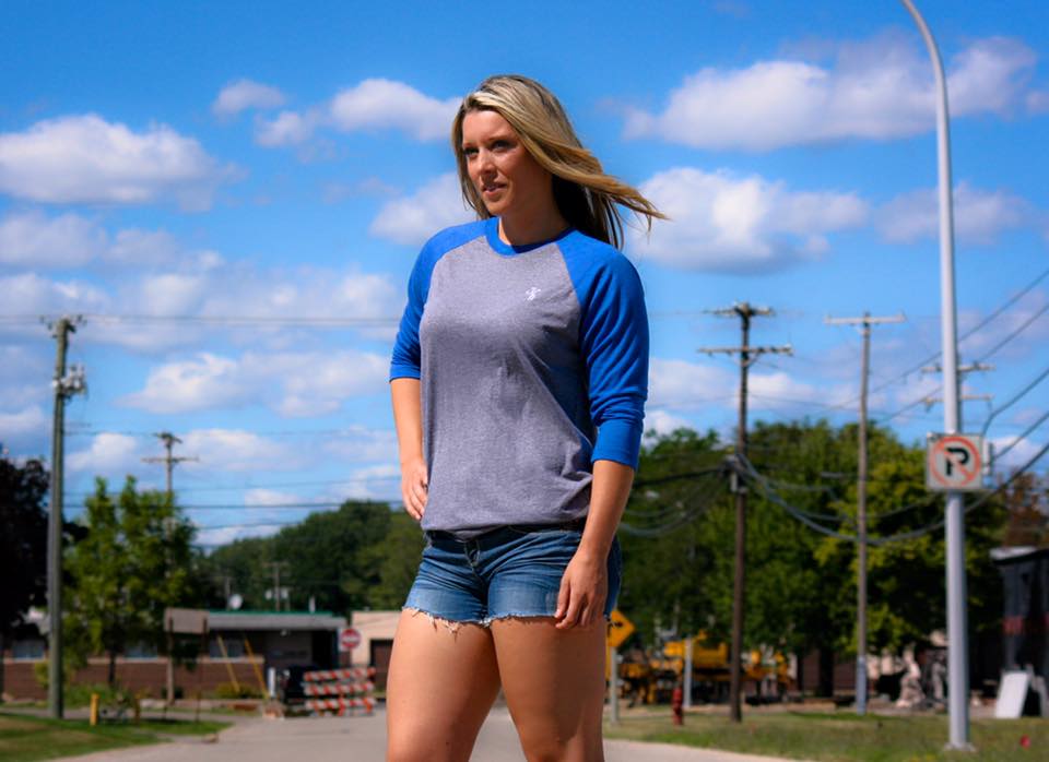Woman standing in the street in cut off shorts and blue grey raglan. 