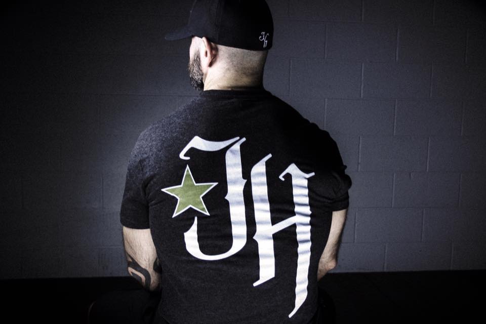 Man sitting on a bench looking away with a black tshirt with JH logo on it. 
