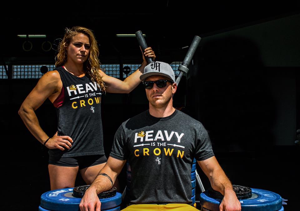 Man and woman at a stack of weights in a shirt that reads; "Heavy is the crown." 
