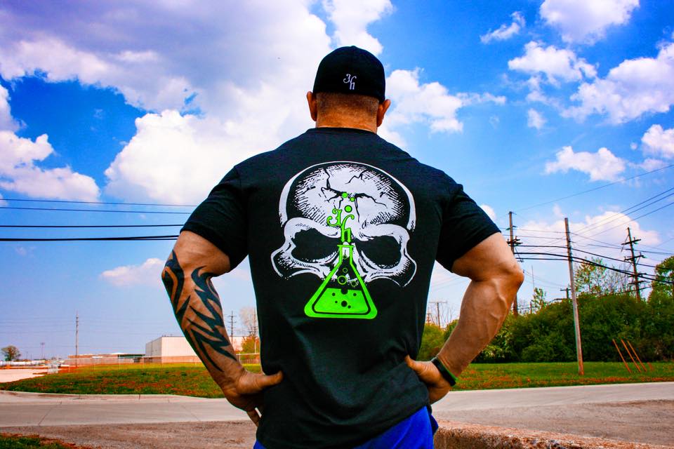 Man standing outside with back to the camera wearing a black shirt with a skull and beaker on it. 