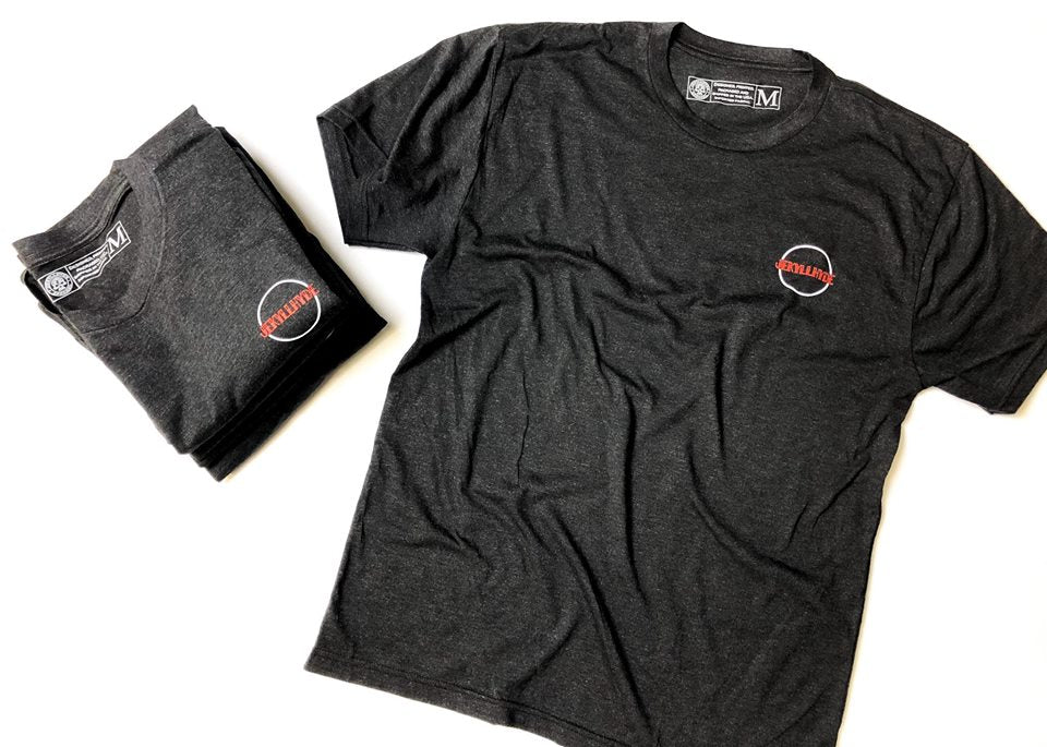 Black tshirt with logo on the left chest laying on the ground. 
