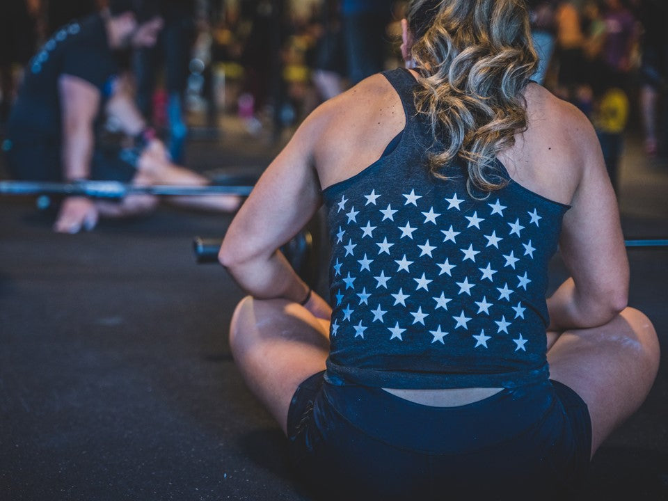 A woman sitting on the ground in a black tank top with stars on the back of it. 