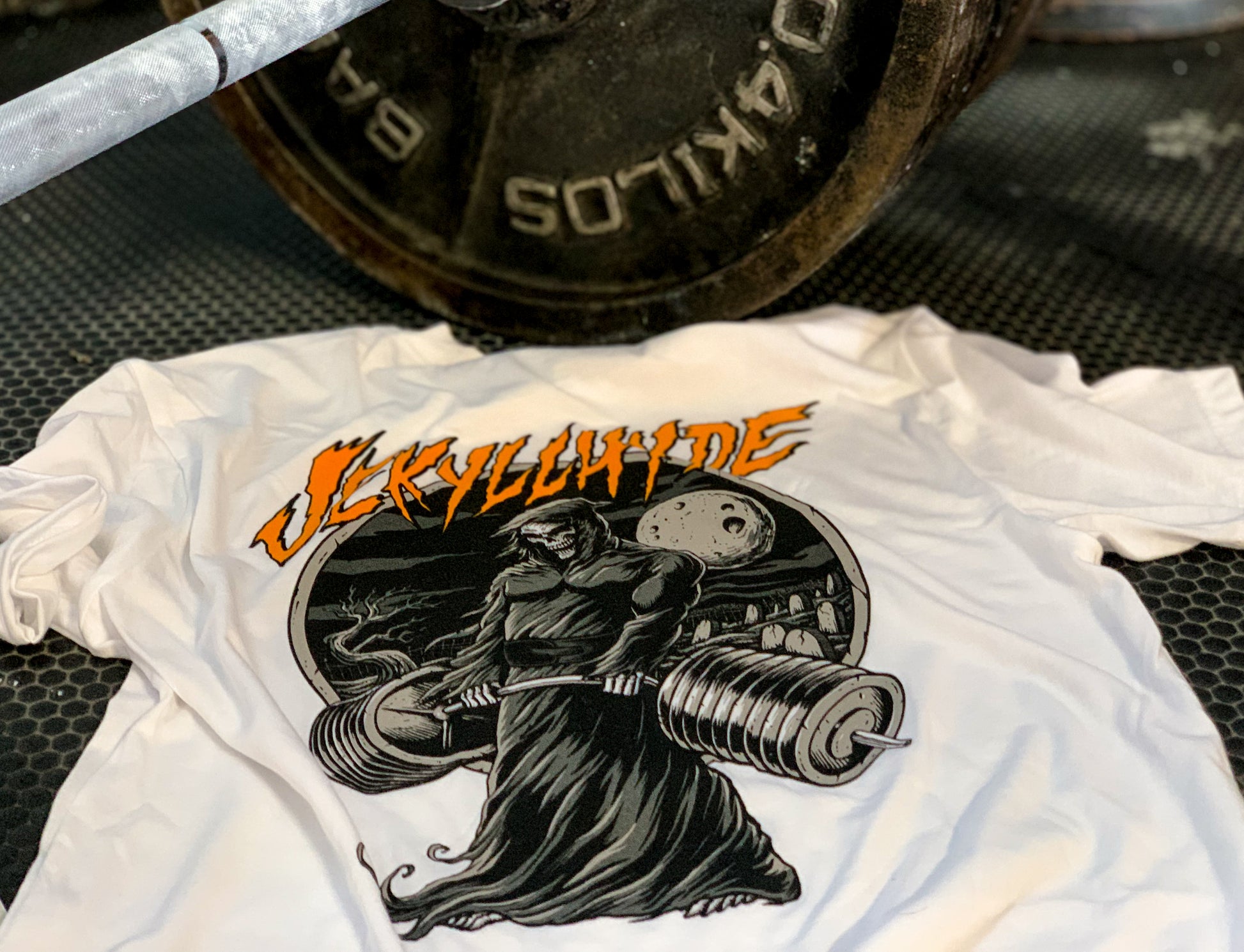 White shirt on the ground next to a barbell. 