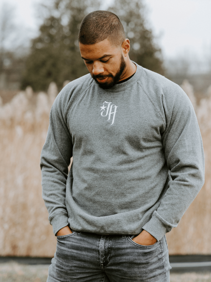 Man standing in a field looking down wearing a grey crewneck sweatshirt. 