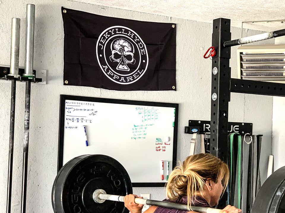 A black gym flag with a skull on it hanging on the wall of a garage gym.