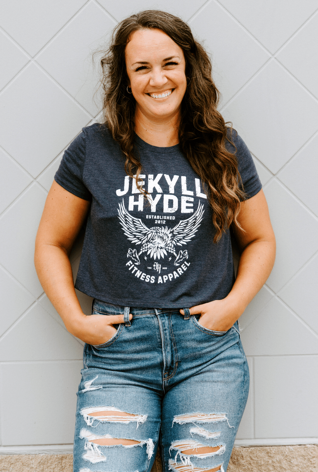 Woman standing against a wall in a blue crop top with an eagle on it. 