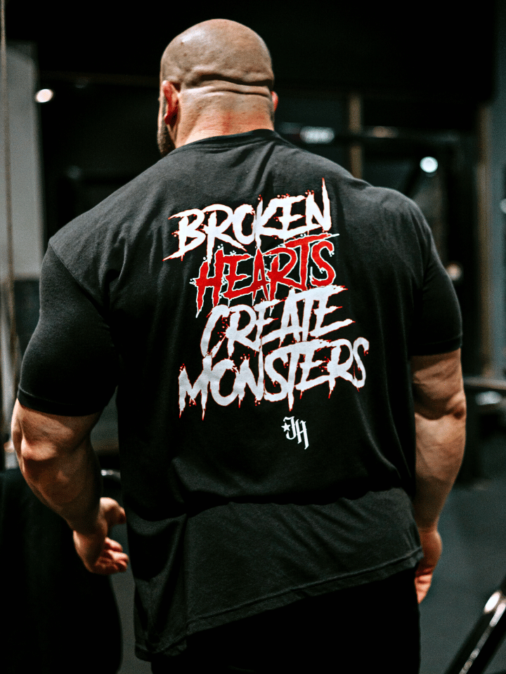A muscular man standing with his back to the camera with a tshirt that reads "Broken hearts create monsters"