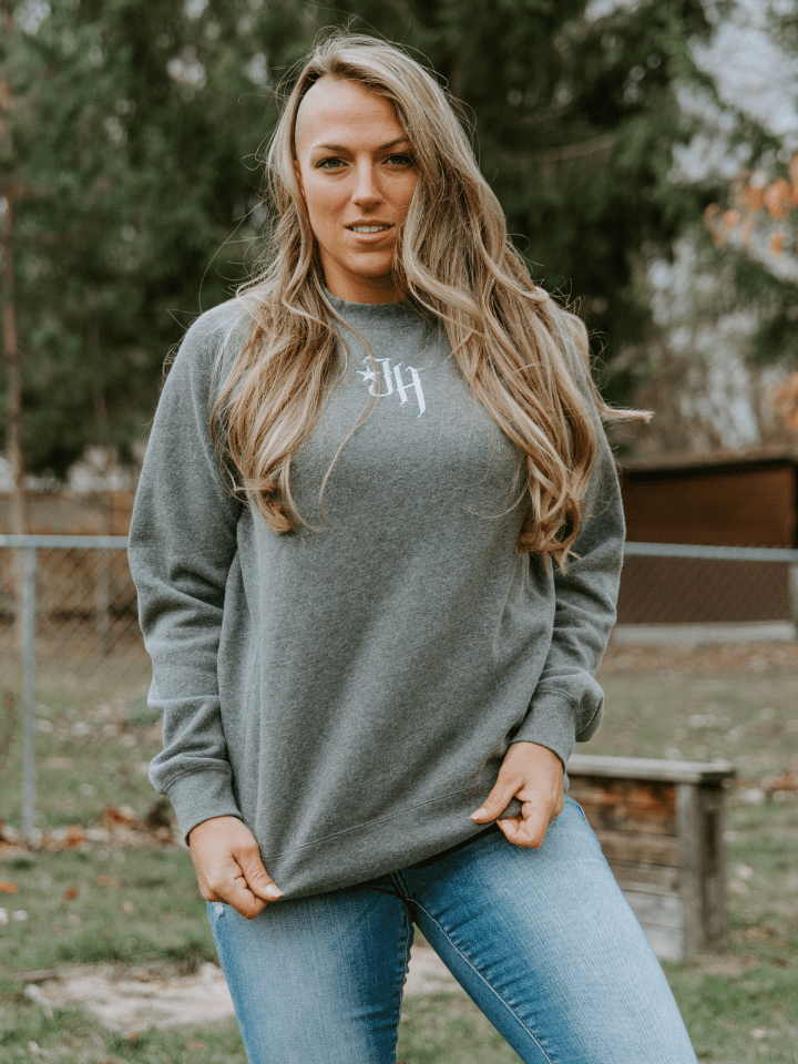 Woman standing in a yard wearing a grey crewneck sweatshirt.