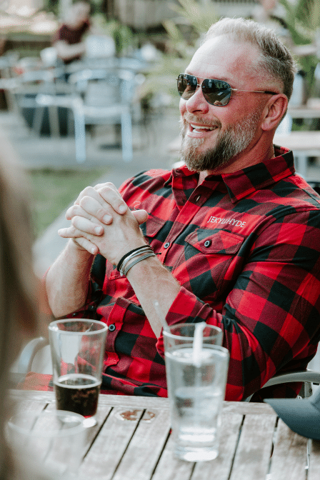 Man in red flannel sitting at a table of drinks. 