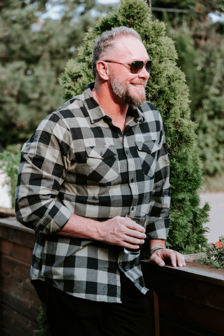 Man in green flannel, smiling, holding a beer. 