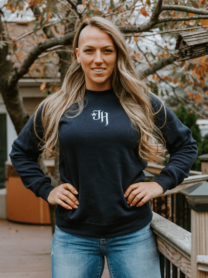 Woman standing on a deck with her hands on hips wearing a navy crewneck sweatshirt. 
