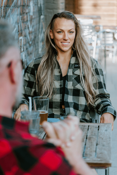 Woman in green flannel siting at a table looking into the camera. 