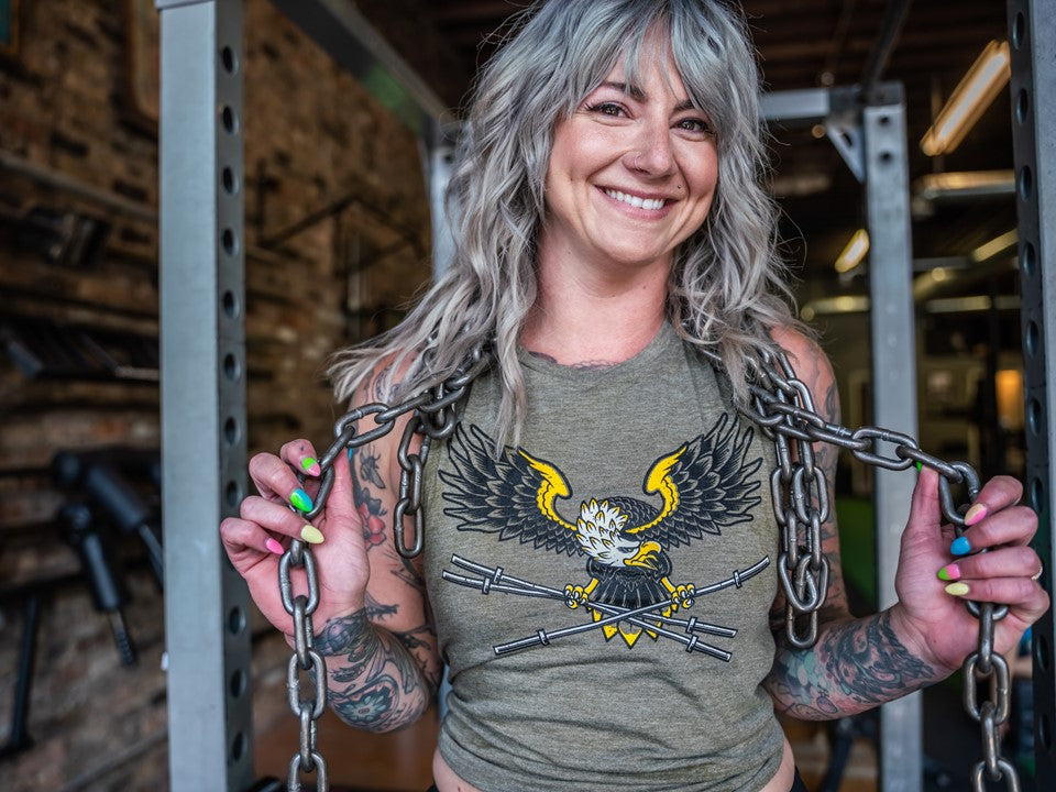 Woman smiling at the camera wearing a shirt with an eagle and barbells on it. 
