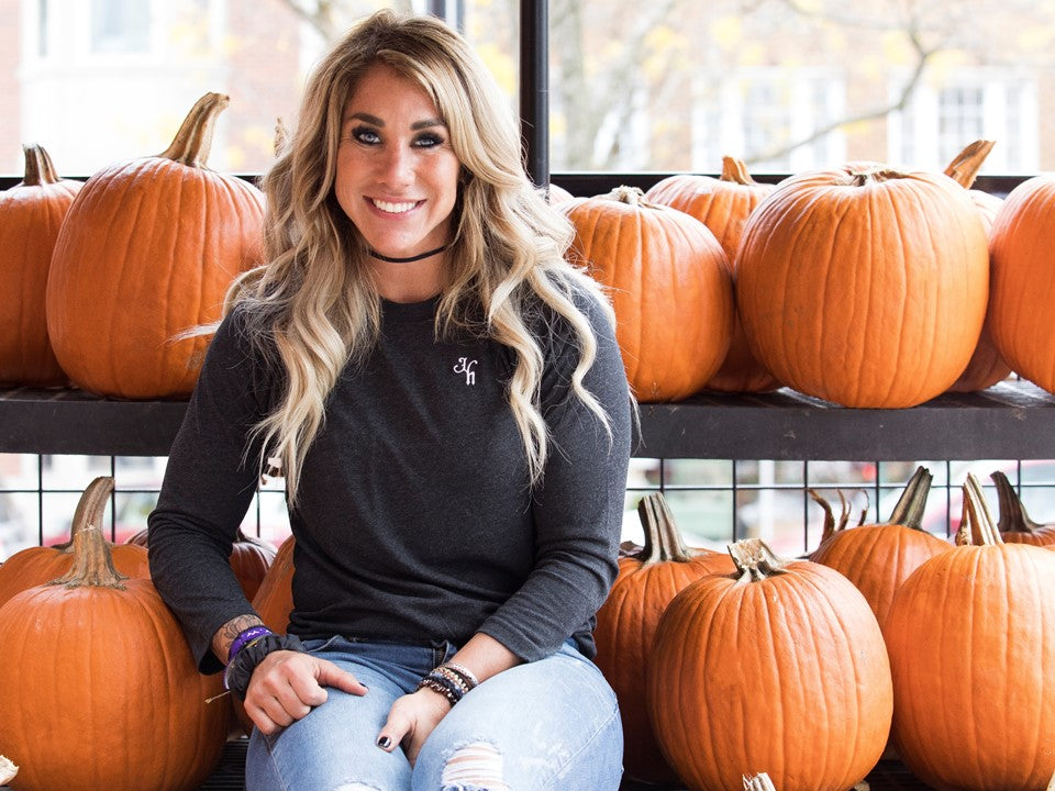 Woman sitting next to a bunch of pumpkins in a black raglan. 