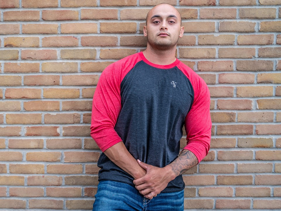 Man leaning against a brick wall in black and red raglan. 