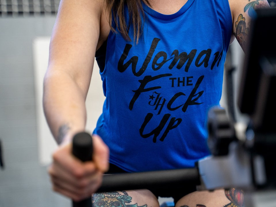 A close up of a blue muscle tee with the words "Woman the F*ck up" printed on it. 