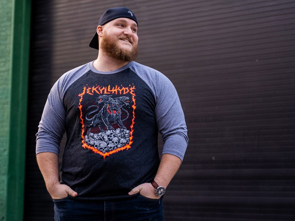 man standing near a garage bay door wearing a raglan with skulls and a cerberus. 