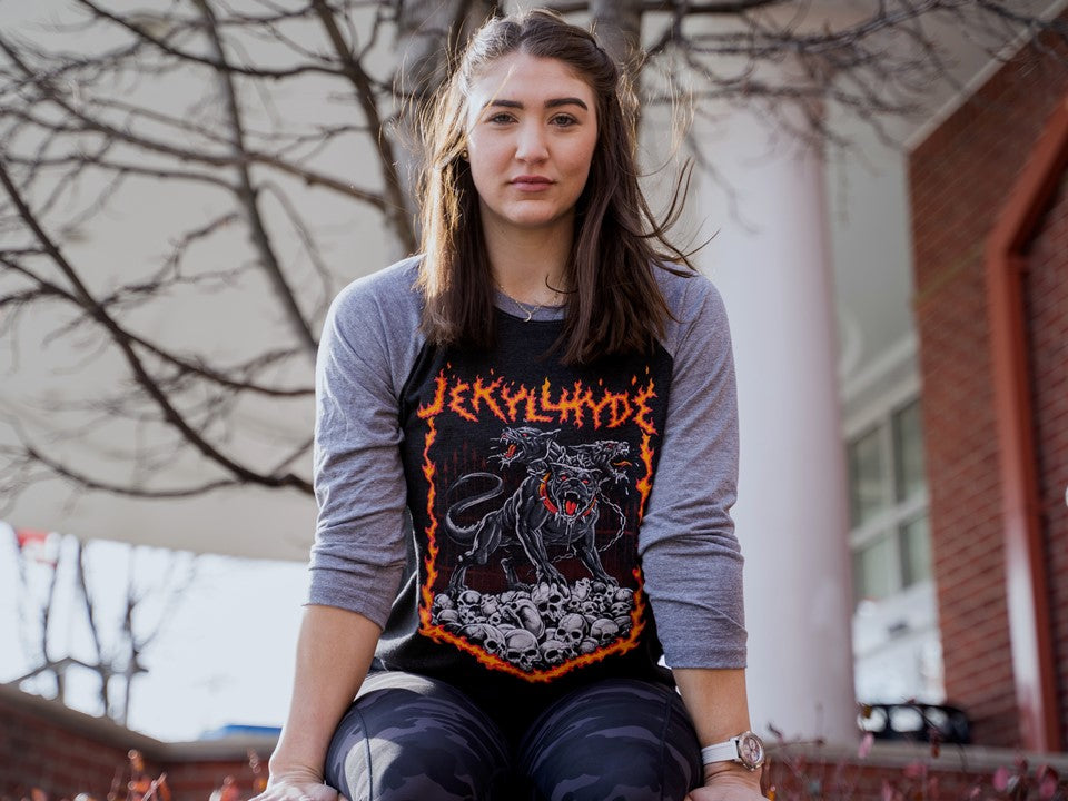 Woman staring into the camera wearing a raglan with skulls and Cerberus on it. 