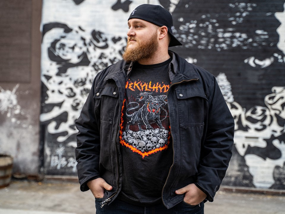 A big, muscular man looking off to the side wearing a tshirt with skulls and Cerberus on it. 