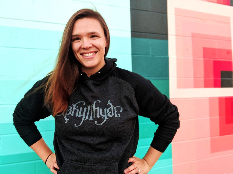 Woman in a black hoodie standing next to a colorful wall. 