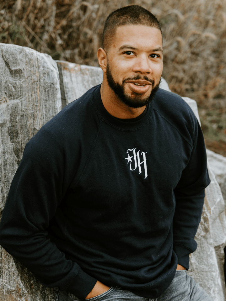 Man looking up and the camera wearing a navy crewneck sweatshirt. 