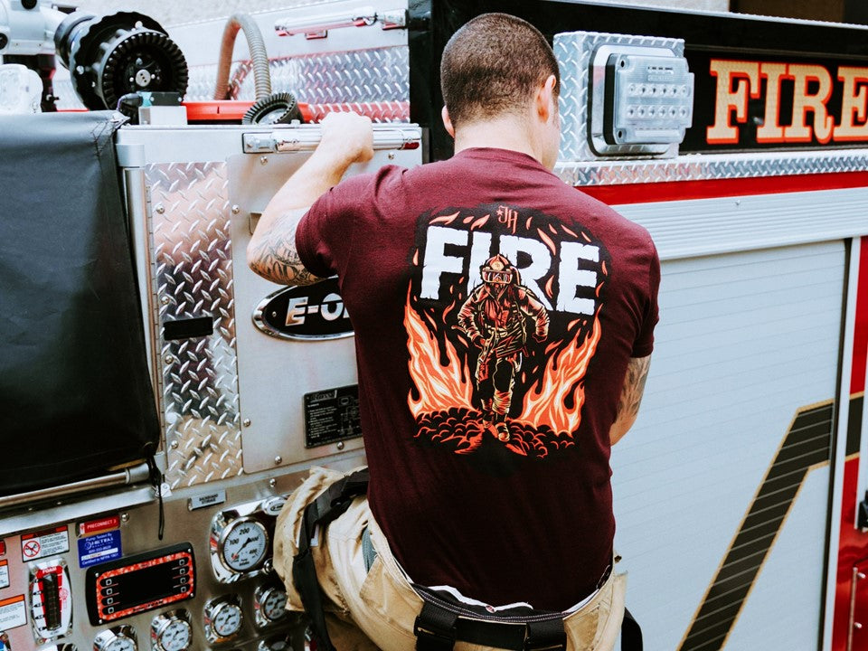 man climbing a fire truck in a maroon tshirt. 